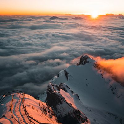 Sunset over snowy mountain peaks above a sea of clouds.