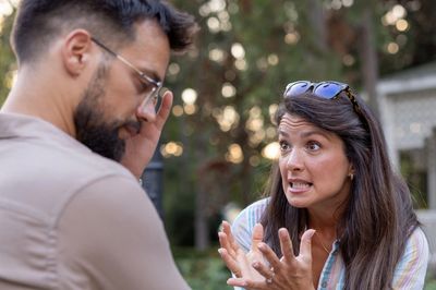 Woman pleading with man who looks stressed outdoors.