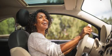 A joyful woman driving a car with a sunroof on a sunny day.