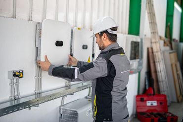 Technician inspecting commercial solar inverters and electrical equipment.