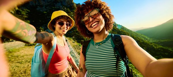 Two people smiling outdoors on a sunny day, holding drinks.