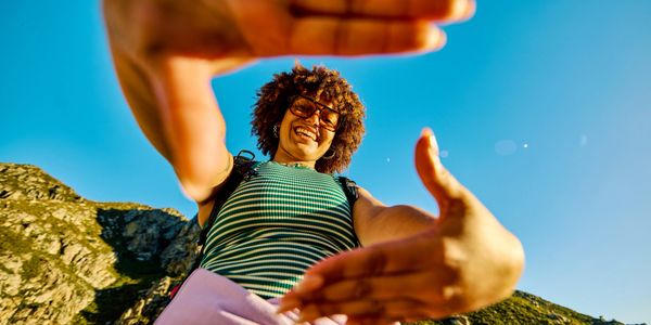 Person framing the sky with their hands while smiling outdoors.