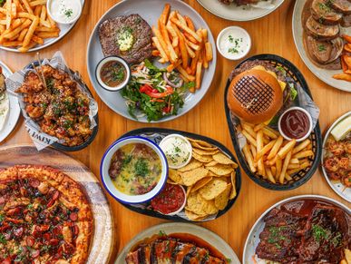 Table full of diverse delicious food including pizza, burgers, fries, and salads.