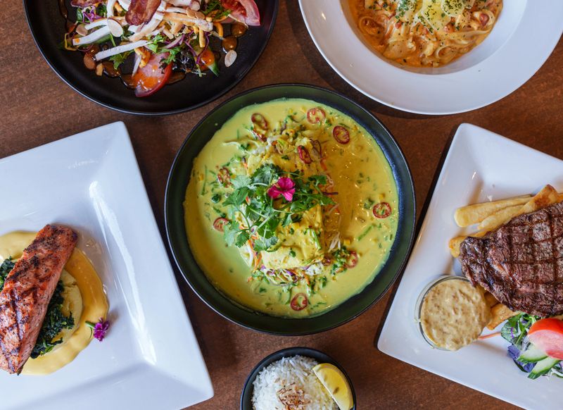 Stew fish with coconut milk in a bowl on the table along with grilled meat, horizontal top view from above.