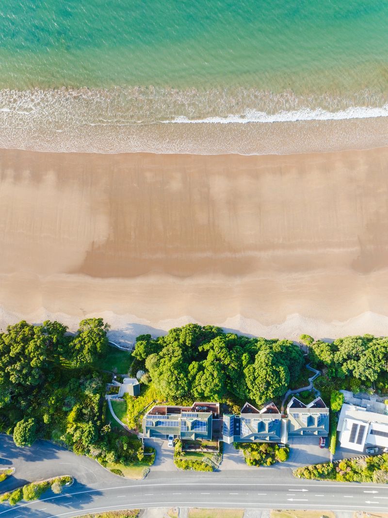 Drone aerial view of suburban residential houses next to the sea, coastal neighborhood along a serene sandy beach.