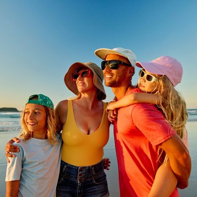 Family enjoying a sunny beach day together, smiling and wearing hats and sunglasses.