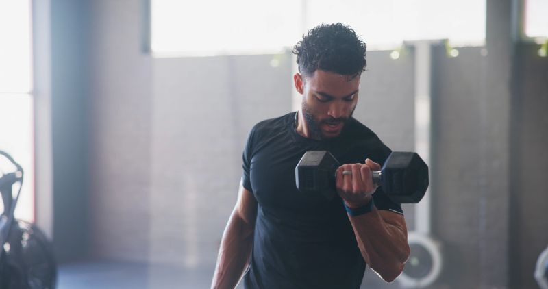 Fitness, man or dumbbell in gym for weightlifting, strong arm muscle development or intense workout. Body builder, exercise or sweating with weight for strength training, commitment or sport activity