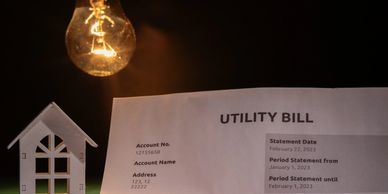 Illuminated bulb above a utility bill and a small house model.