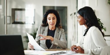 Two professional women discussing documents in an office.