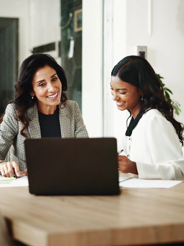 Two women smiling while working on a laptop.