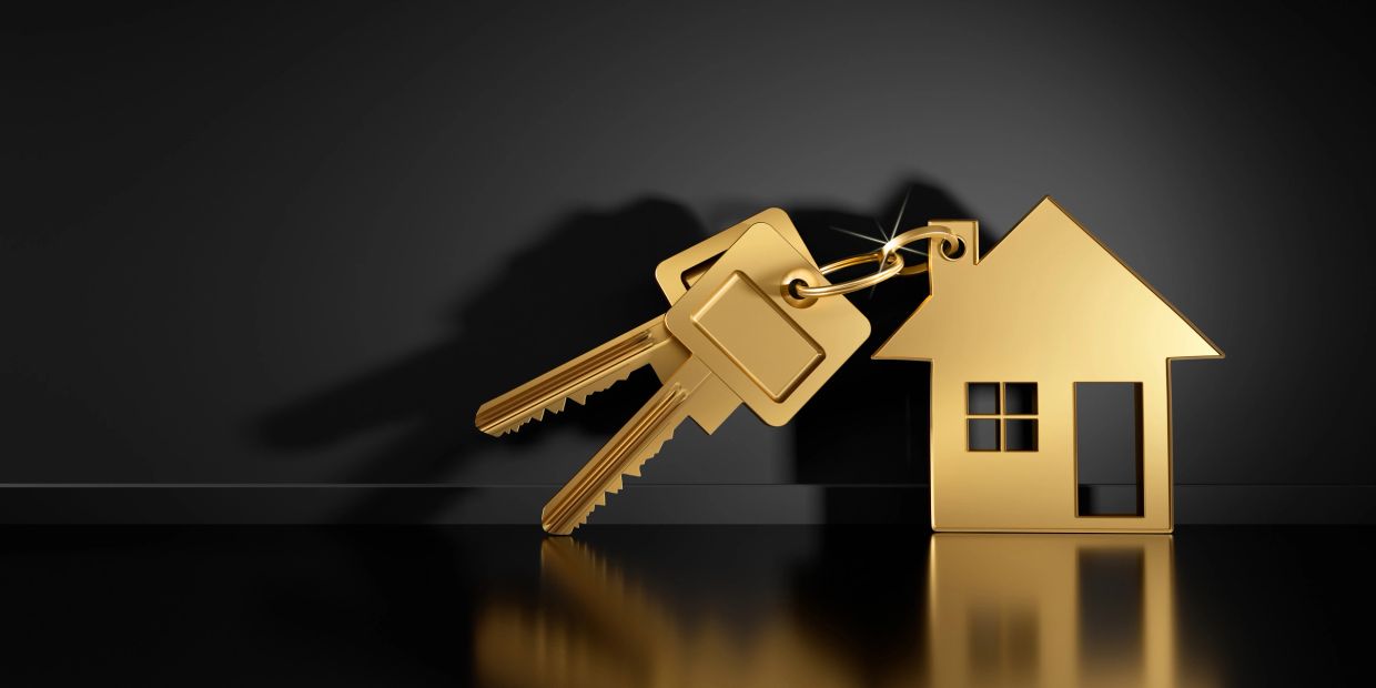 Golden house keychain with two keys on a reflective surface for a real estate lawyer closing.
