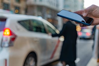 Person using a smartphone near a car in a city street.
