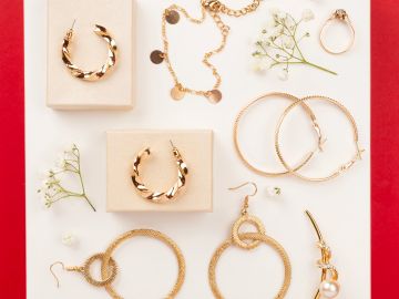 A collection of gold earrings and rings with delicate white flowers on a white and red background.