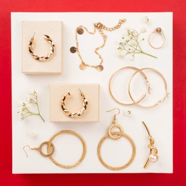Collection of gold earrings and ring on white display with flowers.