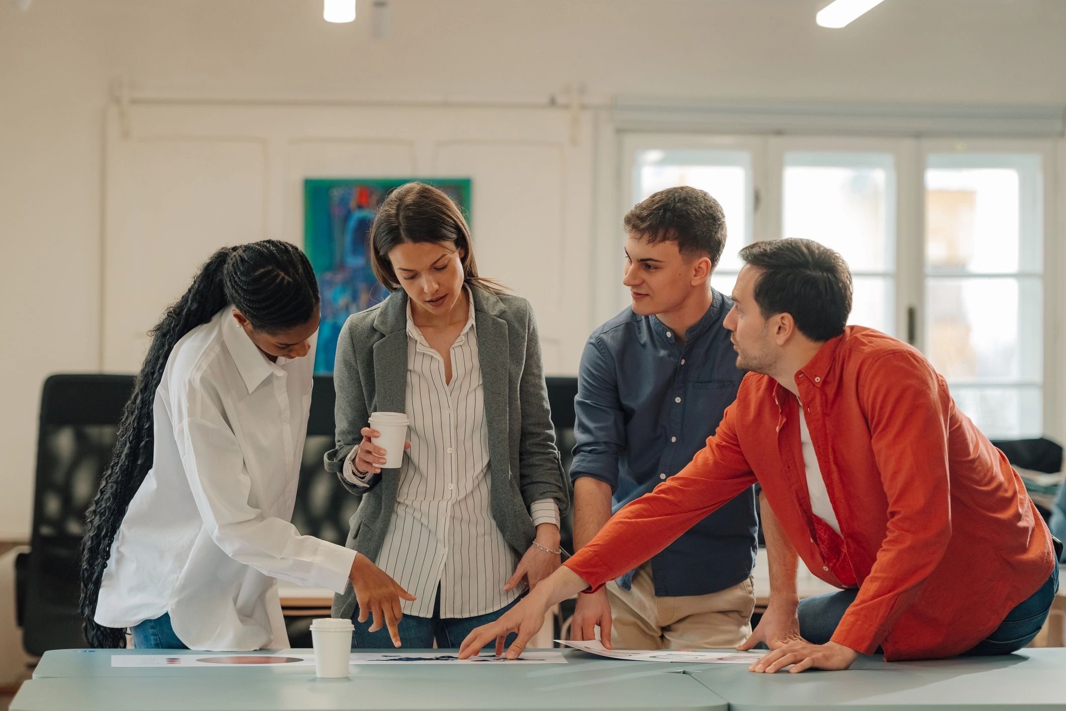 Four colleagues discuss work documents in a bright office.