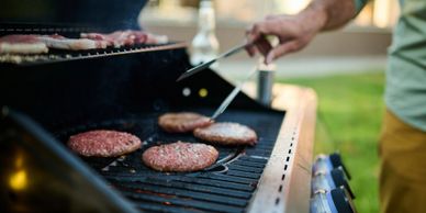 Person grilling multiple hamburger patties on an outdoor barbecue grill.