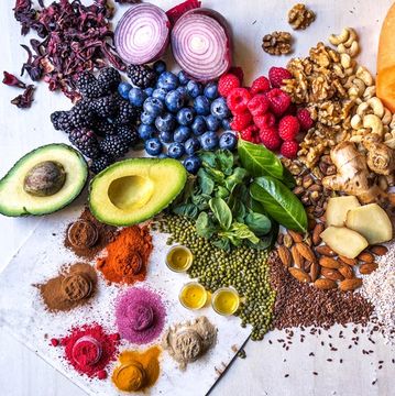 A colorful array of fresh fruits, nuts, spices, and herbs arranged on a white surface.