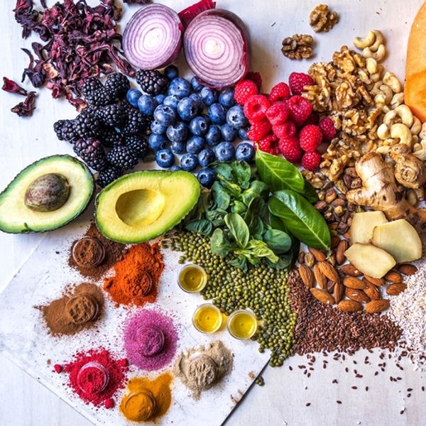Colorful assortment of fresh fruits, nuts, spices, and greens laid out on a surface.