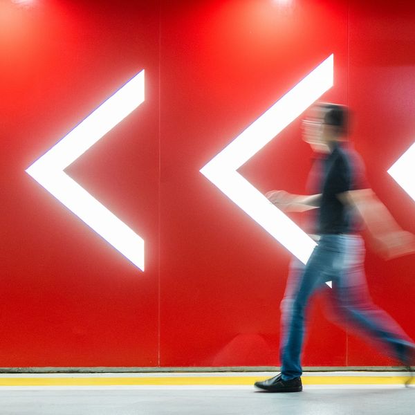 Blurred person walking past large illuminated left arrow signs on a red wall.