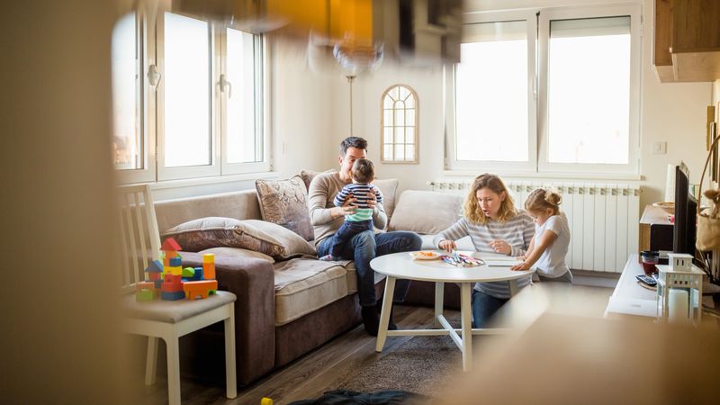 A cozy modern living room scene with a family spending quality time together. The room is filled with natural light and contains a mix of contemporary and playful elements.