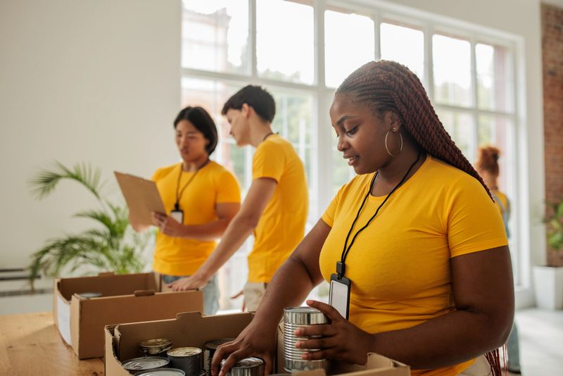 Team of young volunteers, representing different cultures and backgrounds, collaborate to sort food donations into boxes at a charity center. The image showcases the power of teamwork in addressing food insecurity.