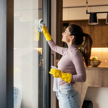 Woman cleaning a window wearing yellow gloves and holding a spray bottle.