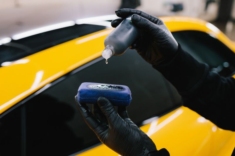 Process of pouring ceramic liquid from bottle on sponge to apply a protective nano layer on car. Detailing service worker applies ceramic protective liquid on sponge close-up