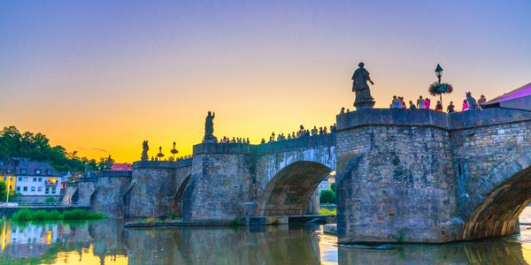Historic stone bridge with statues at sunset over calm water.