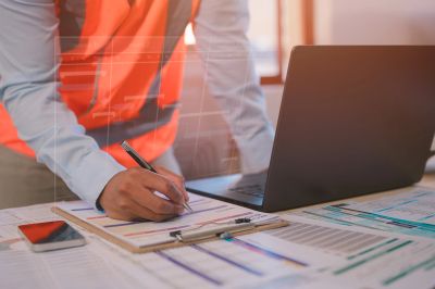 Engineer working on project plans with laptop and documents.