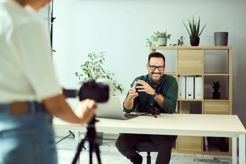 Confident man smiling during video recording at tidy office with camera and microphone.