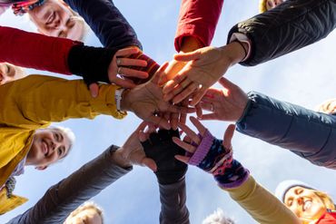 Group of people joining hands in a unity circle outdoors.