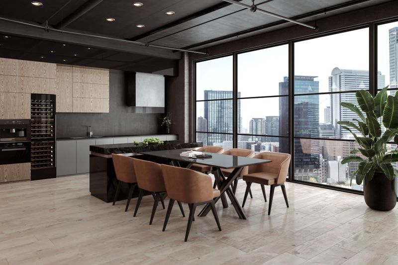 Modern high-rise dining area with a cityscape view. A black dining table with brown upholstered chairs complements the wood-paneled kitchen and marble accents.