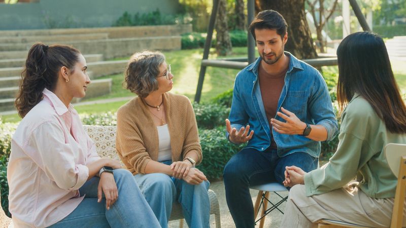 Diverse group of people engaging in supportive group therapy session, sharing personal stories and advice to promote mental health and recovery in park. Mental health community concept.