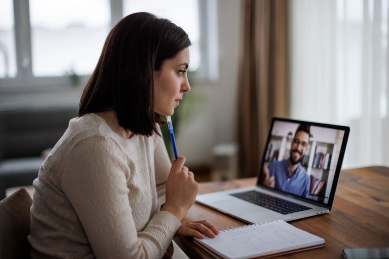 Thoughtful woman attending an online class, taking notes while listening to her virtual instructor