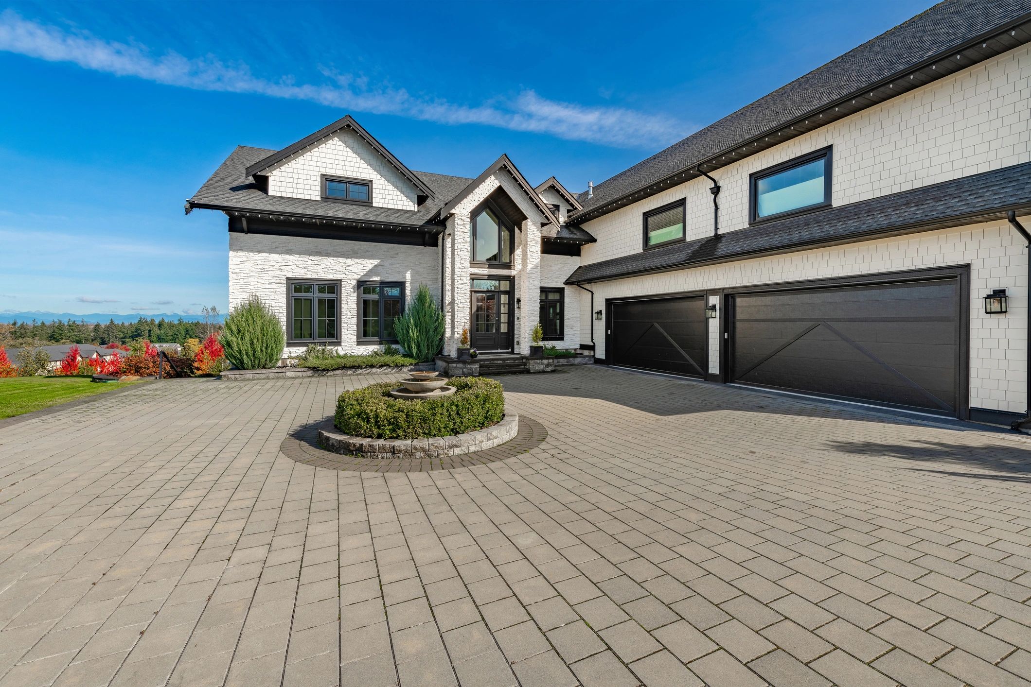 Large modern house with black garage doors and a circular fountain.