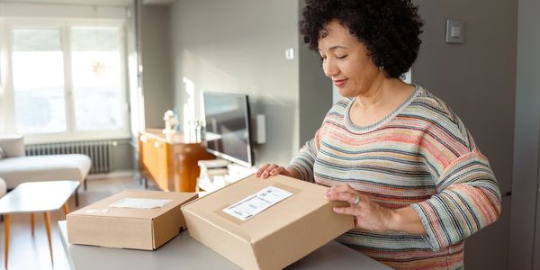 A woman opening a package at home with another package nearby.