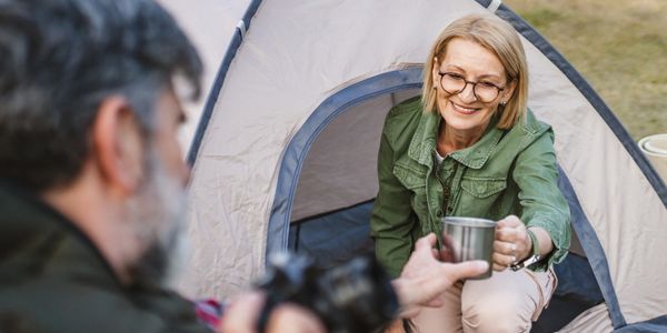 A woman happily shares a drink while camping in a tent.