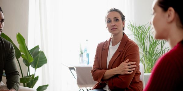 People engaged in a serious group discussion in a cozy room with plants.