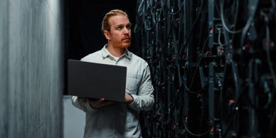 Man with laptop working in server room.