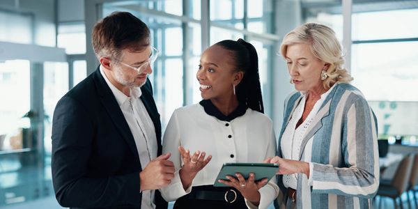 Three professionals discussing work using a tablet in a modern office.