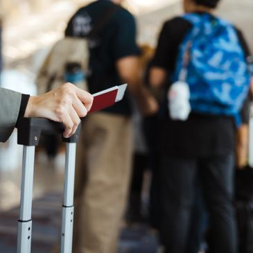 Traveler holding a passport and luggage handle in an airport line.