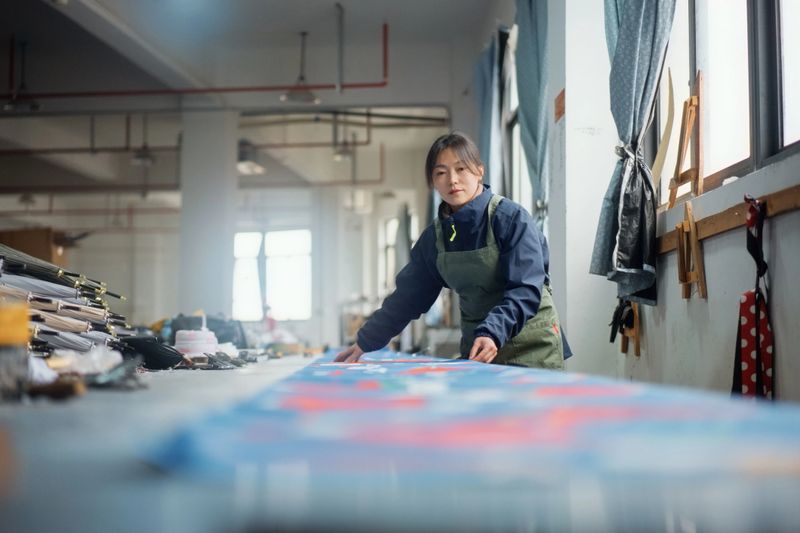 Female workers in the pattern-making workshop are cutting cloth with scissors.