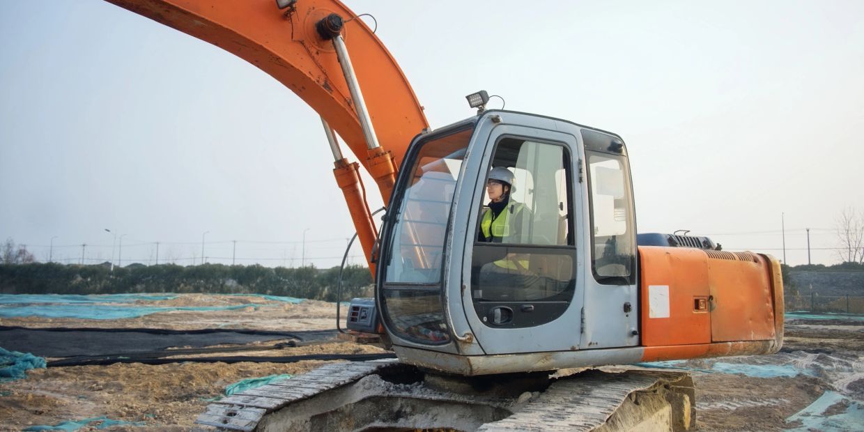 Person operating an orange excavator at a construction site.