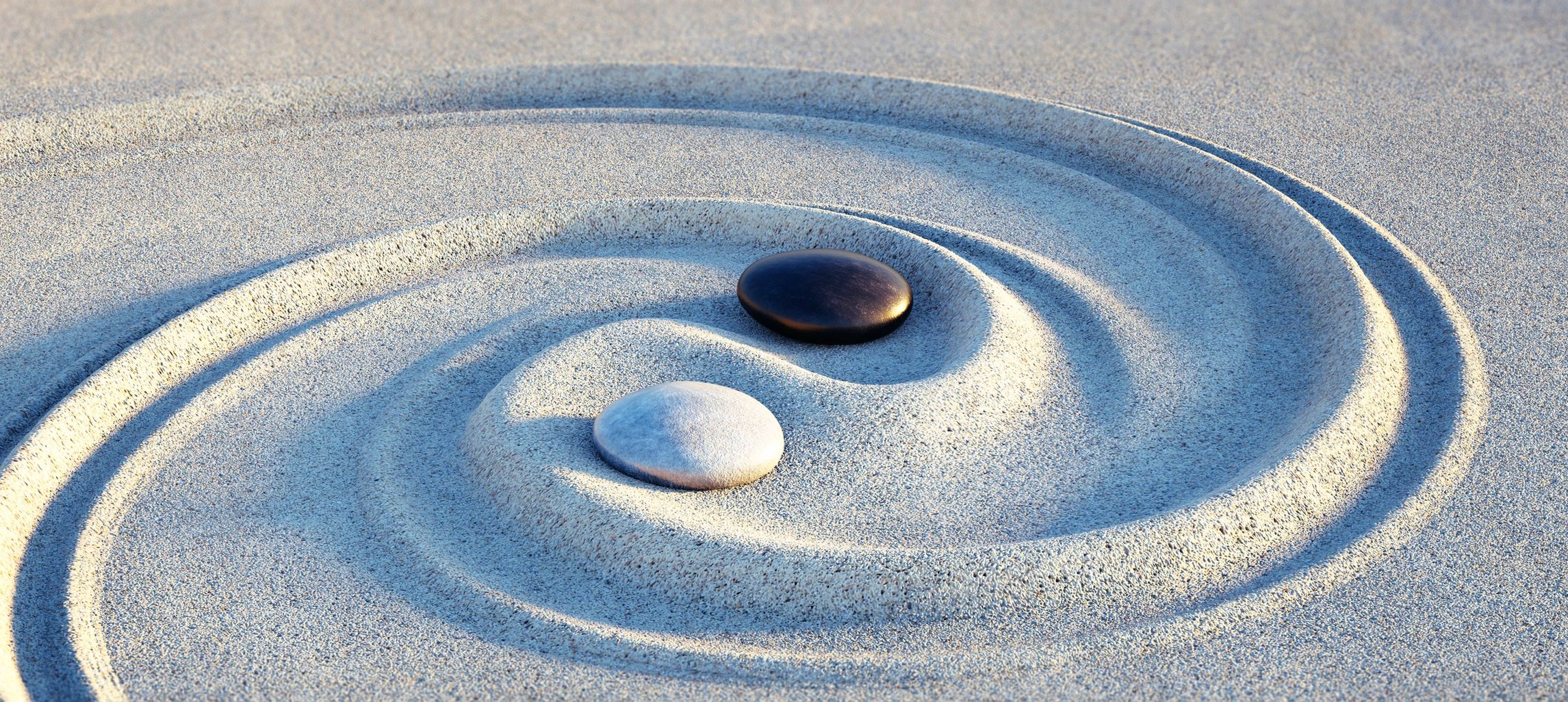 Black and white stones in a yin-yang pattern on textured sand.