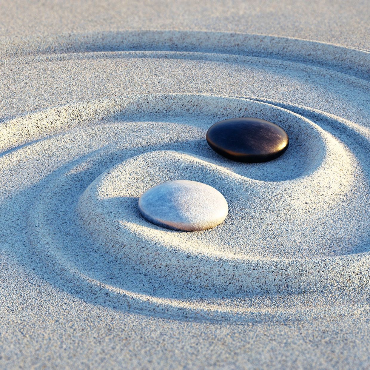 Black and white stones in sand forming a yin-yang symbol.