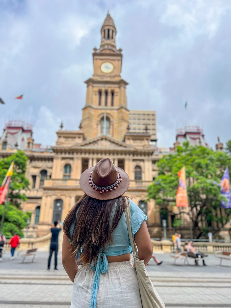 Smiling woman in casual attire poses in front of historic building. Tourist in summer clothes enjoying city tour.