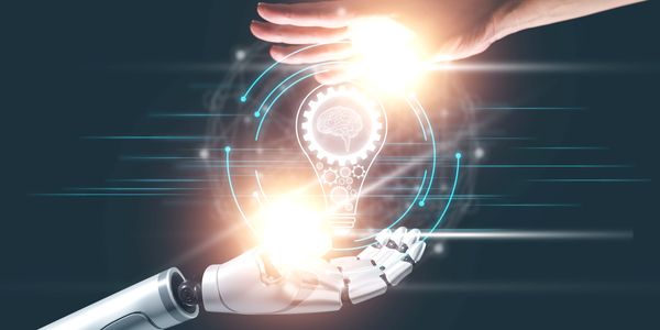 Human and robot hands creating a glowing light bulb symbolizing innovation.