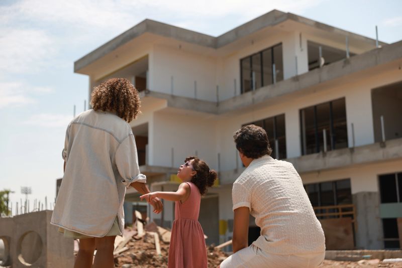 Happy parents with daughter standing at new construction building  Family standing  outside house under construction.family of three gathers and inspecting the construction of their new home.