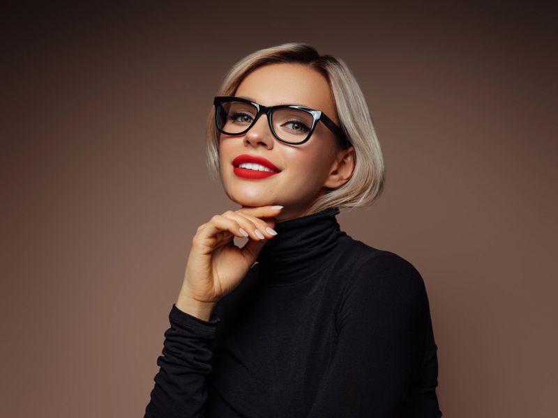A stylish woman wearing glasses, red lipstick, and a black outfit poses elegantly. Her confident expression and sophisticated fashion choice create a modern and fashionable aesthetic perfect for promoting style, beauty, or lifestyle concepts.