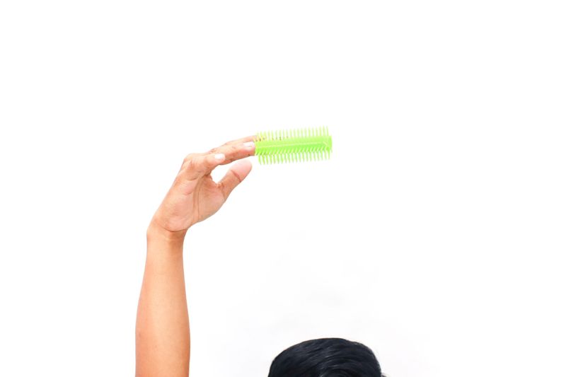 Close up image of a hand holding a neon green hair roller against a white background.